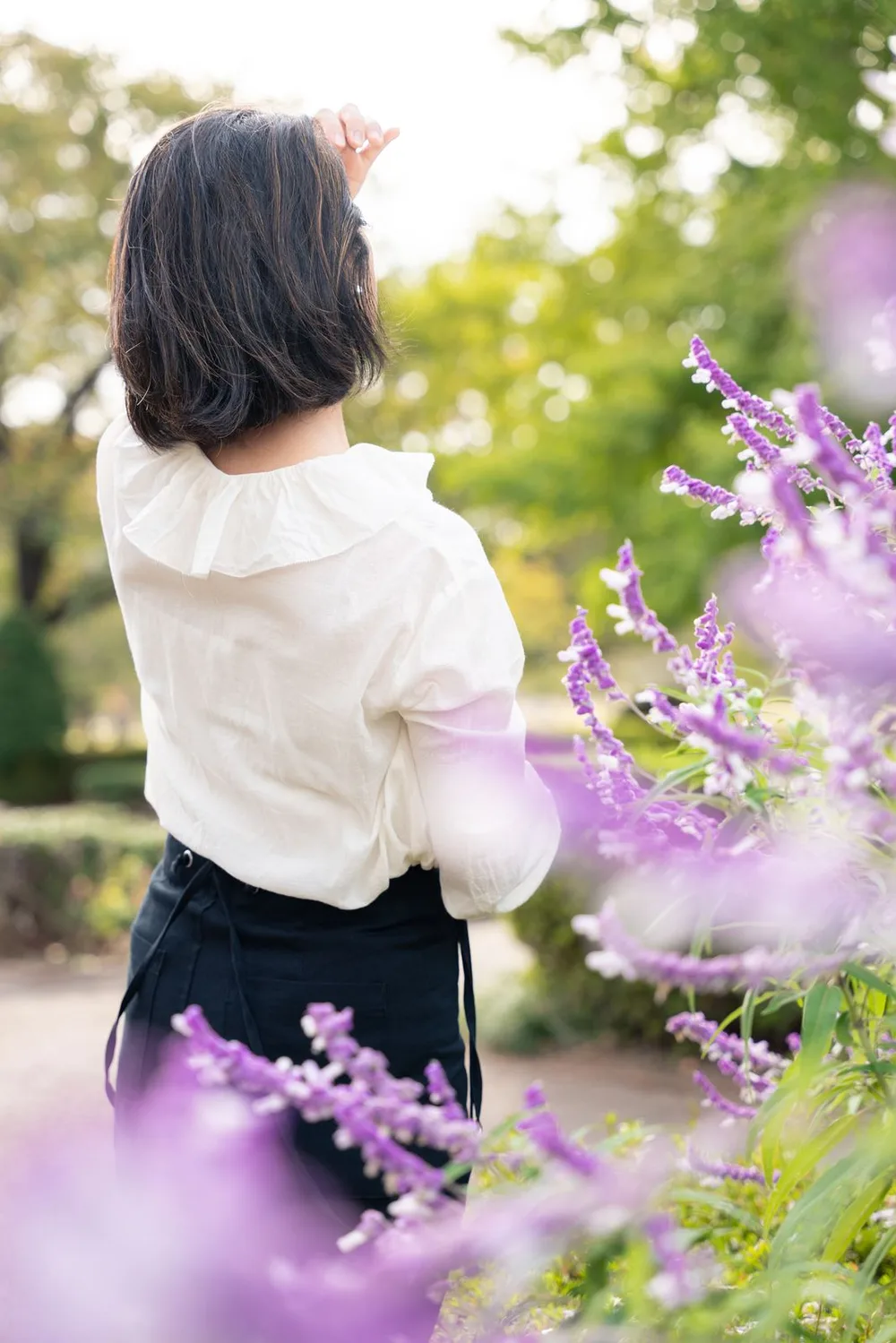 花の向こうで空に手を伸ばす女性の後ろ姿